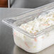 A Vollrath clear polycarbonate food pan filled with food on a counter.