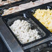 A Vollrath black polycarbonate food pan on a counter in a buffet with various types of food.