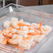 A clear plastic food pan with shrimp on a counter.
