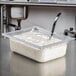 A Vollrath clear polycarbonate food pan with food and a spoon inside on a counter.