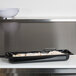 A black Vollrath Super Pan food tray on a counter full of food.