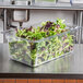 A Vollrath clear polycarbonate food pan filled with lettuce on a counter.