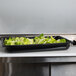 A Vollrath black polycarbonate food pan filled with lettuce on a counter.