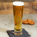 A Libbey Pinnacle Pilsner glass of beer on a table with pretzels.