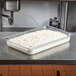 A clear Vollrath polycarbonate food pan on a counter filled with white food.