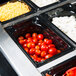 A row of Vollrath 1/4 size black polycarbonate food pans filled with food on a counter.