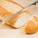 An American Metalcraft stainless steel serrated knife cutting a piece of bread.