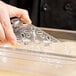 A hand using a Vollrath clear polycarbonate drain tray to fill a plastic container at a salad bar.