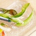 A clear polycarbonate Vollrath drain tray with a green pepper and onion on it, with tongs and a spoon.