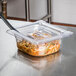 A Vollrath 1/6 size clear polycarbonate plastic slotted cover on a food container on a counter.