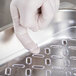 A person wearing gloves holds a Vollrath clear plastic drain tray.