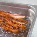 A Vollrath clear polycarbonate food pan drain tray holding bacon strips over a metal tray filled with bacon.