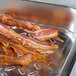 A Vollrath clear polycarbonate drain tray with cooked bacon on a hotel counter.