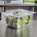 A plastic container with green and red lettuce in a Vollrath clear lid.