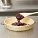 A wooden spoon pouring red liquid into a glass pie pan.