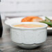 A close up of a Tuxton bright white china bouillon cup filled with soup on a table.