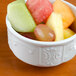 A Tuxton bright white china bowl filled with fruit on a table.