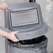 A person's hand opening a grey Continental dome top trash can lid.