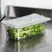 A Carlisle clear plastic lid on a container of green lettuce on a counter.