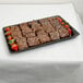 A tray of brownies with strawberries on top on a white embossed paper table cover.
