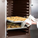 A person holding trays of food in a Cambro double compartment tray and sheet pan carrier in an oven.