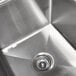 A close-up of the drain in an Advance Tabco stainless steel three compartment sink.