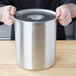 A person holding a silver container with a Vollrath stainless steel lid.