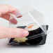 A hand holding a clear plastic container with a sushi inside.