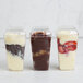 A row of Fineline plastic cups with clear dome lids filled with chocolate, strawberry, and yogurt desserts.