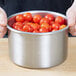 A person holding a Vollrath stainless steel pot of tomatoes.