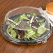 A clear plastic dome lid on a plastic container with salad inside.