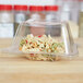A clear plastic Fineline bowl lid on a plastic container with food inside.
