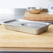 A Vollrath stainless steel deli pan on a cutting board.