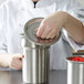 A woman in a white chef's jacket opening a Vollrath stainless steel container.