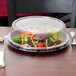 A salad in a Fineline clear plastic container with a clear dome lid on a table.