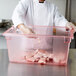 A chef in a white coat holding a Carlisle red food storage box full of raw meat.