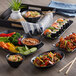 A black rectangular melamine tray with bowls and plates of Asian cuisine dishes on a table.