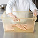 A chef holding a Carlisle yellow plastic food storage container filled with raw chicken.
