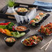 A black Elite Global Solutions rectangular melamine platter with bowls of rice, noodles, and shrimp and vegetable dishes on a table.