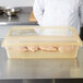 A chef in a white coat putting a yellow Carlisle lid on a large plastic food storage container with chicken inside.