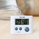 A Taylor white digital kitchen timer on a wooden table.