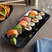 A black rectangular melamine tray with sushi on a table.