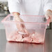A person in gloves putting raw meat into a Carlisle red plastic food storage box.