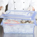 A chef in a white coat holding a Carlisle blue plastic container with ice and fish in it.