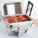 A Maximillian rectangular chafer with food in a stainless steel pan on a table outdoors.