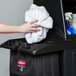 A person's arm with a white towel in a black bag on a Rubbermaid housekeeping cart.