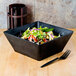 An American Metalcraft black melamine serving bowl filled with salad on a table.