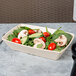 A rectangular Papyrus-colored melamine bowl filled with salad with tomatoes, cucumbers, and spinach.