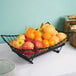 A Tablecraft Grand Master Transformer rectangular black metal basket filled with oranges and apples on a table.