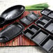 A group of black rectangular Elite Global Solutions melamine trays on a bamboo surface.